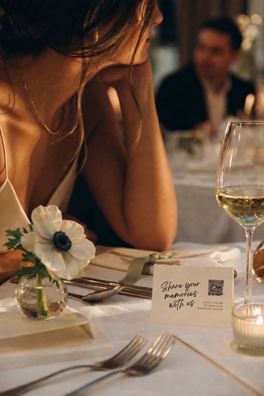 Wedding guest at a table with the Share Your Memories QR card, anemone, and wine glass