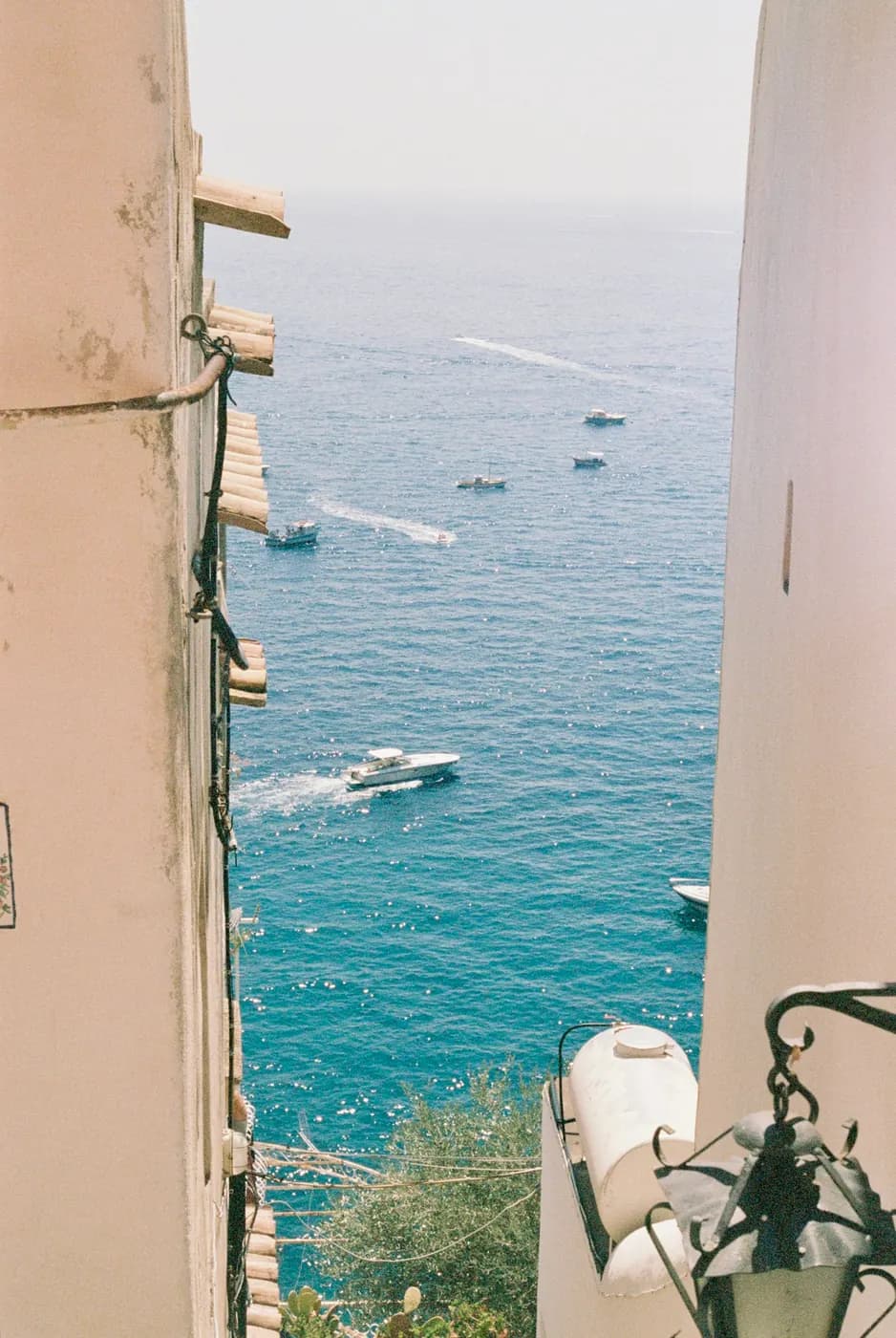 Una vista estrecha entre las luminosas paredes de Positano hacia un mar turquesa salpicado de barcos